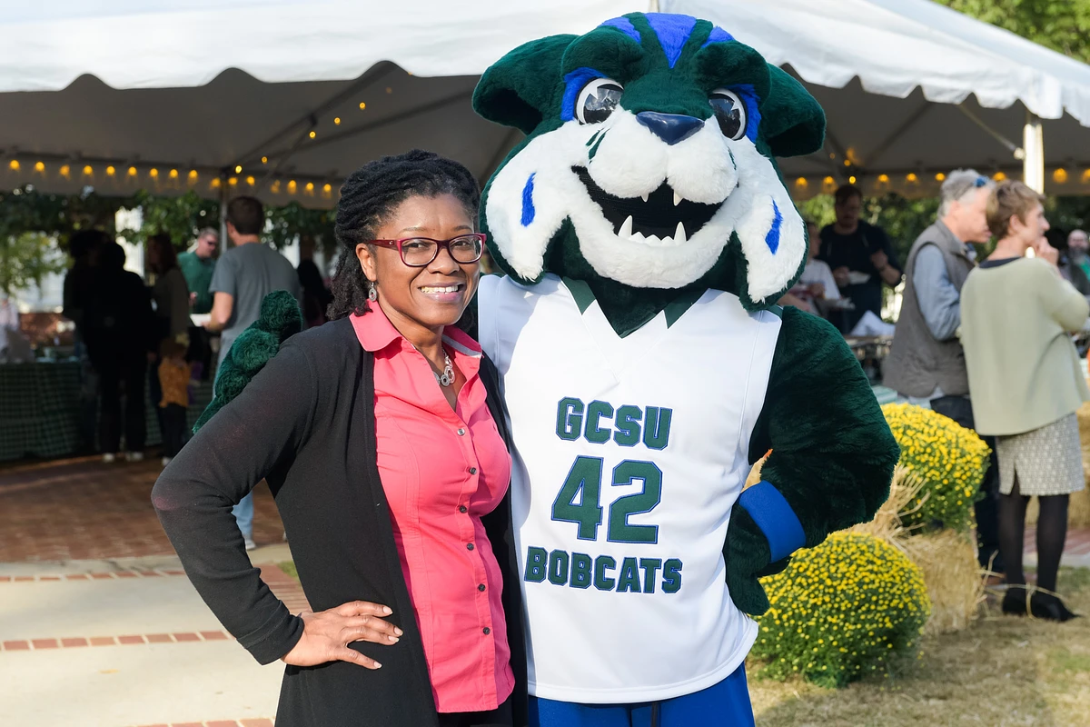 A woman smiles beside a friendly mascot in a "GCSU 42 Bobcats" jersey at an outdoor event.
